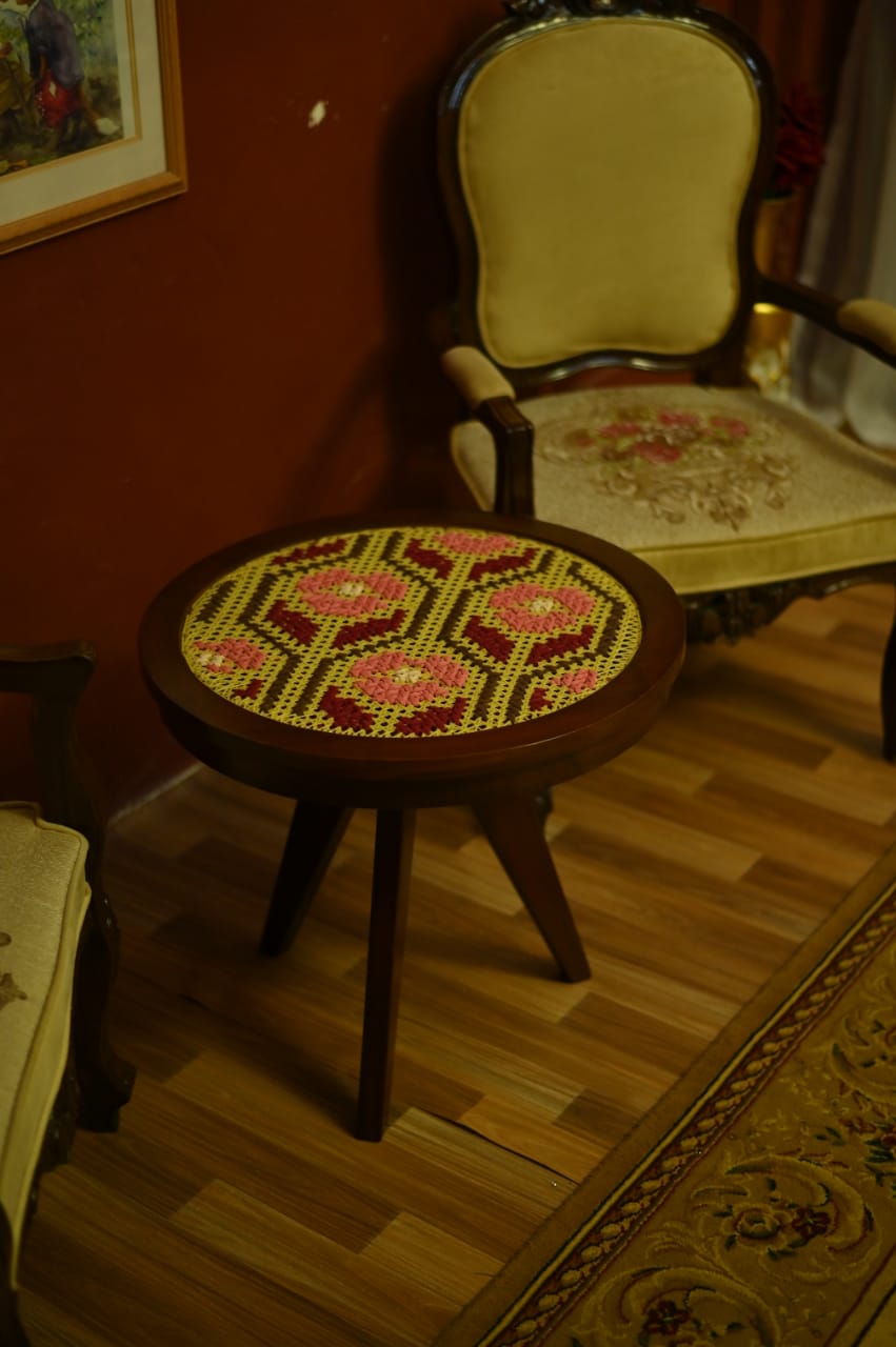 Wooden stool with floral patterned seat in a room with a chair and painting on the wall.